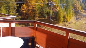 A wooden deck with a table and chairs, overlooking a mountainous landscape with autumn-colored trees and a ski lift in the background. - Ski-in/ski-out & foot of the slopes, 6th floor, balcony, tv, 24m², La Plagne (La Plagne)