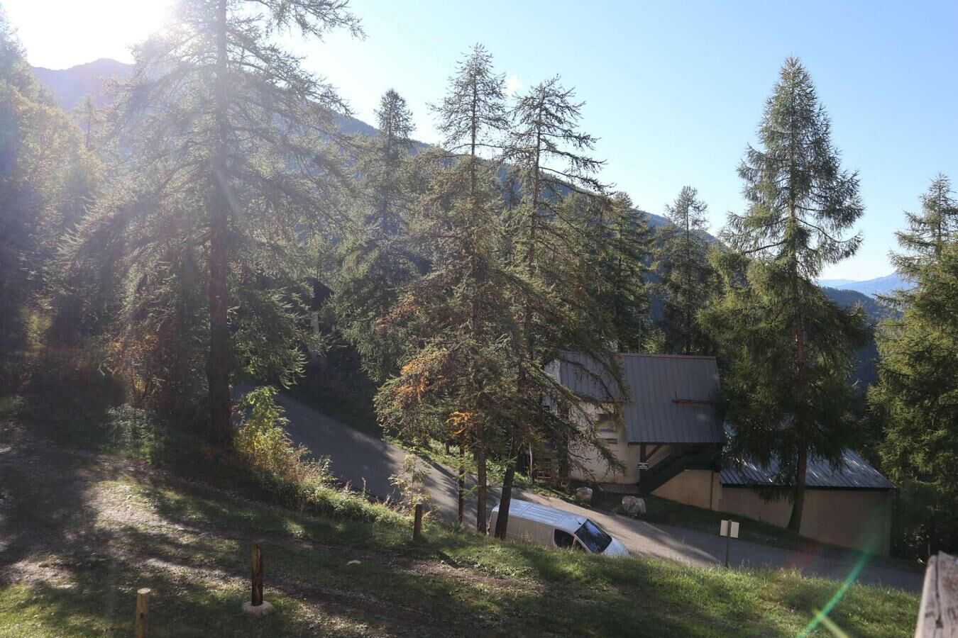 Ein Gebäude mit einem geneigten Dach, umgeben von dichtem Wald und Bergen im Hintergrund.
