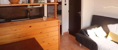 Une cuisine compacte avec des meubles en bois et un plan de travail, une table à manger et un canapé avec des coussins.