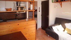 Une cuisine compacte avec des meubles en bois et un plan de travail, une table à manger et un canapé avec des coussins.