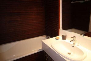 A bathroom with a white sink, a mirror, and a dark wooden wall.