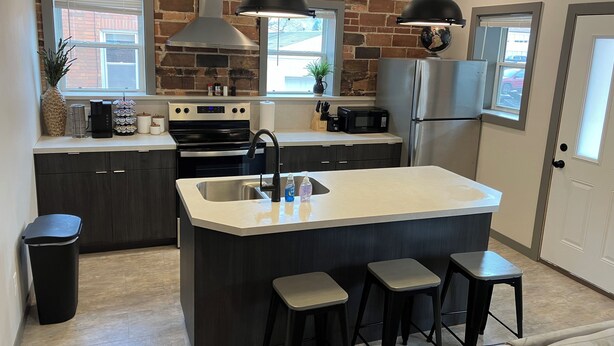A modern kitchen with a central island, dark cabinetry, stainless steel appliances, and pendant lighting.