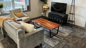 A living room with a sofa, a wooden coffee table, a globe, a TV, and a suitcase.