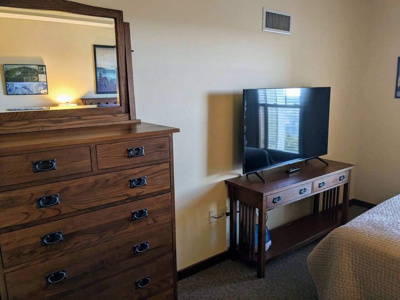 Een hotelkamer met een houten dressoir, een televisie op een standaard en een bed met een sprei.