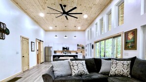 Un salon moderne avec un canapé d’angle gris, des coussins décoratifs à motifs et un plafond en bois agrémenté d’un ventilateur de plafond.