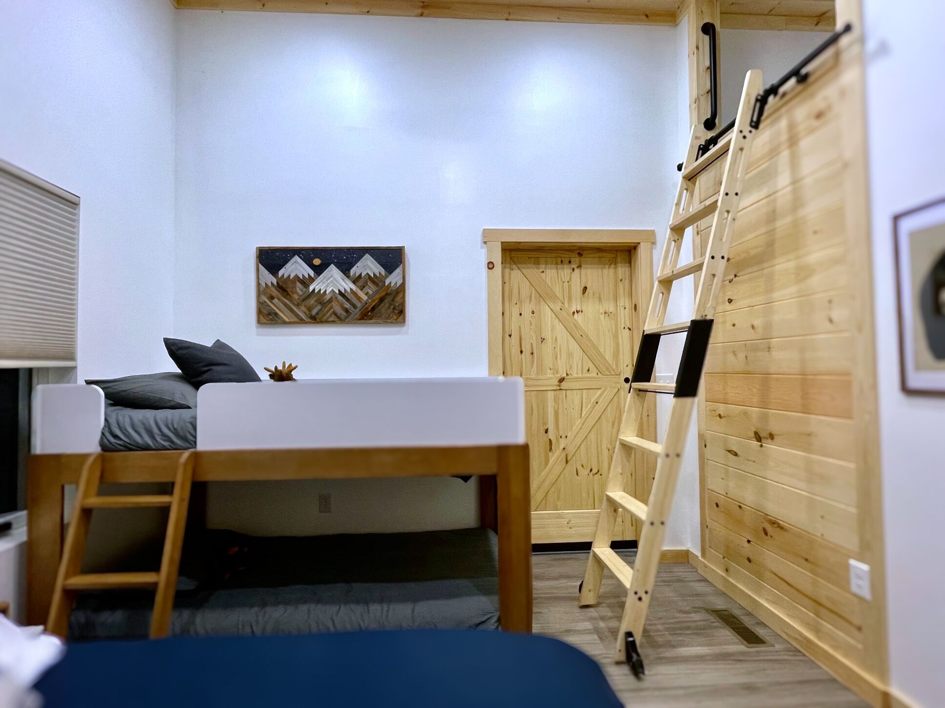 A compact room with a bunk bed, a ladder, a wooden wardrobe, and a framed picture on the wall.
