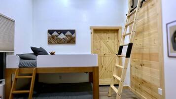 A compact room with a bunk bed, a ladder, a wooden wardrobe, and a framed picture on the wall.