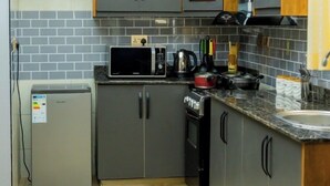 A compact kitchen with grey cabinets, a microwave, a small refrigerator, and a stove. - Cozy Residences Kampala 002 (Kampala)