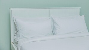 A bed with white bedding and a white headboard against a light green wall. - Cozy Residences Kampala 002 (Kampala)