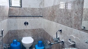 A modern bathroom with a marble floor, a white toilet, a blue bidet, a large bathtub, and a showerhead.