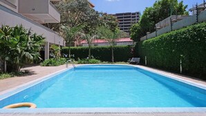 A rectangular swimming pool with a clear blue water surface, surrounded by a low hedge and a few trees.
