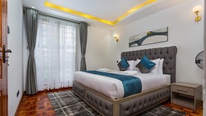 A bedroom with a large bed, a bedside table, a wall-mounted light, and a window with curtains.