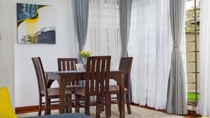 A dining area with a wooden table and chairs, a vase with flowers, and sheer curtains.