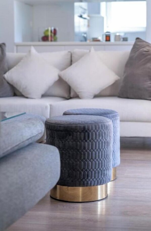A modern living room with a grey sofa, two grey ottomans, and a white couch with multiple cushions.