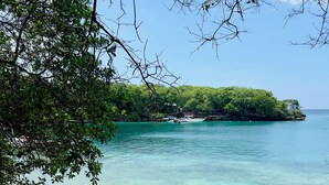 Une plage à l’eau turquoise et limpide, un rivage sablonneux et, au loin, une île couverte de forêts.