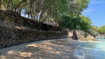 Stroll down the stone wall to a secluded beach, surrounded by lush greenery and calm waters.