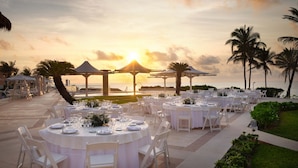 An outdoor dining area with round tables set for a meal, surrounded by palm trees and a sunset view. - All Inclusive Grand Cancun Beachfront Luxury Resort 3-bedroom/3.5 BathVilla. (Cancún)