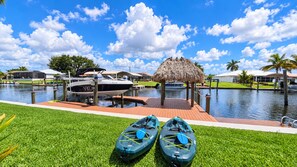 A marina with boats docked, a thatched structure, and kayaks on the grass. - VRCC Villa Sea Breeze - tropical retreat (Cape Coral)