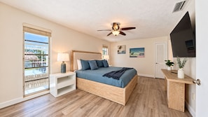 A bedroom with a bed, nightstand, ceiling fan, TV, and a view of a pool. - VRCC Villa Sea Breeze - tropical retreat (Cape Coral)