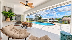 A modern outdoor living area with a pool, wicker furniture, and a ceiling fan.