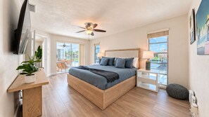 Un dormitorio con cama, mesita de noche, lámpara, ventilador de techo y vistas al exterior.