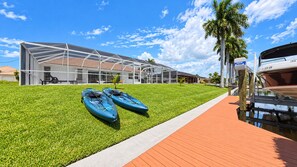 Un edificio moderno con fachada de vidrio, un espacio con césped y kayaks, y un muelle de madera con un bote.