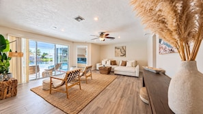 A spacious living room with a sofa, chairs, a coffee table, and a large window overlooking a pool. - VRCC Villa Sea Breeze - tropical retreat (Cape Coral)