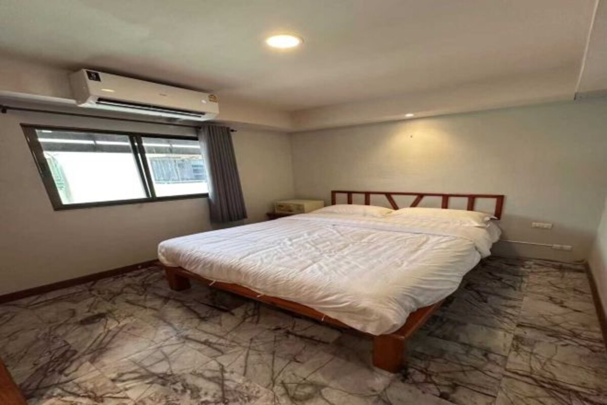 A bedroom with a bed, an air conditioning unit, a window, and a marble-patterned floor.