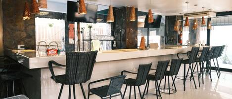 A modern bar area with black wicker chairs, a long counter, and pendant lighting.