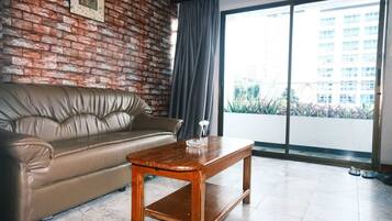 A living room with a leather sofa, a wooden coffee table, a large window with a view of buildings, and a brick wall.