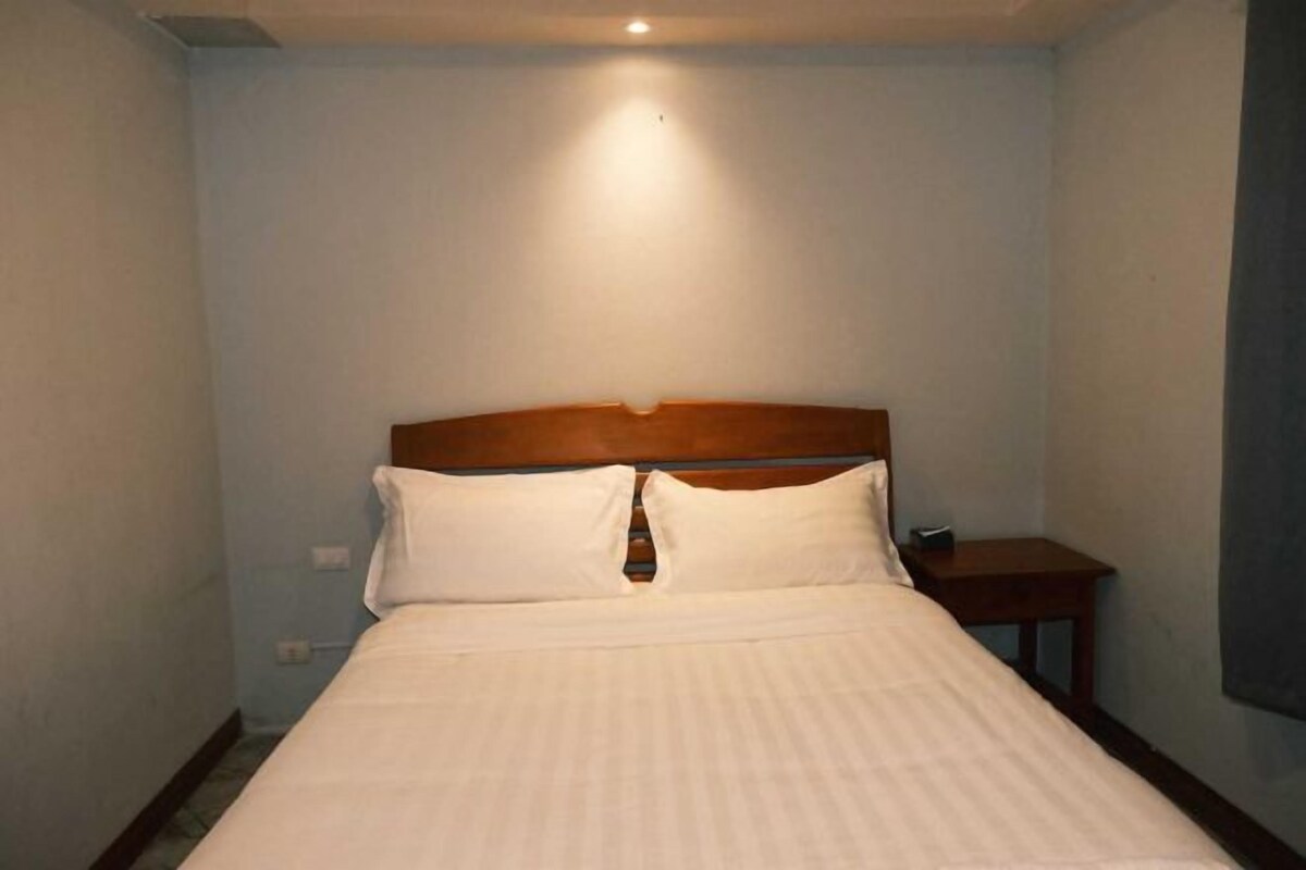 Ein Hotelzimmer mit einem Einzelbett, einem Holz-Kopfteil, einem Nachttisch und einer Wandleuchte.