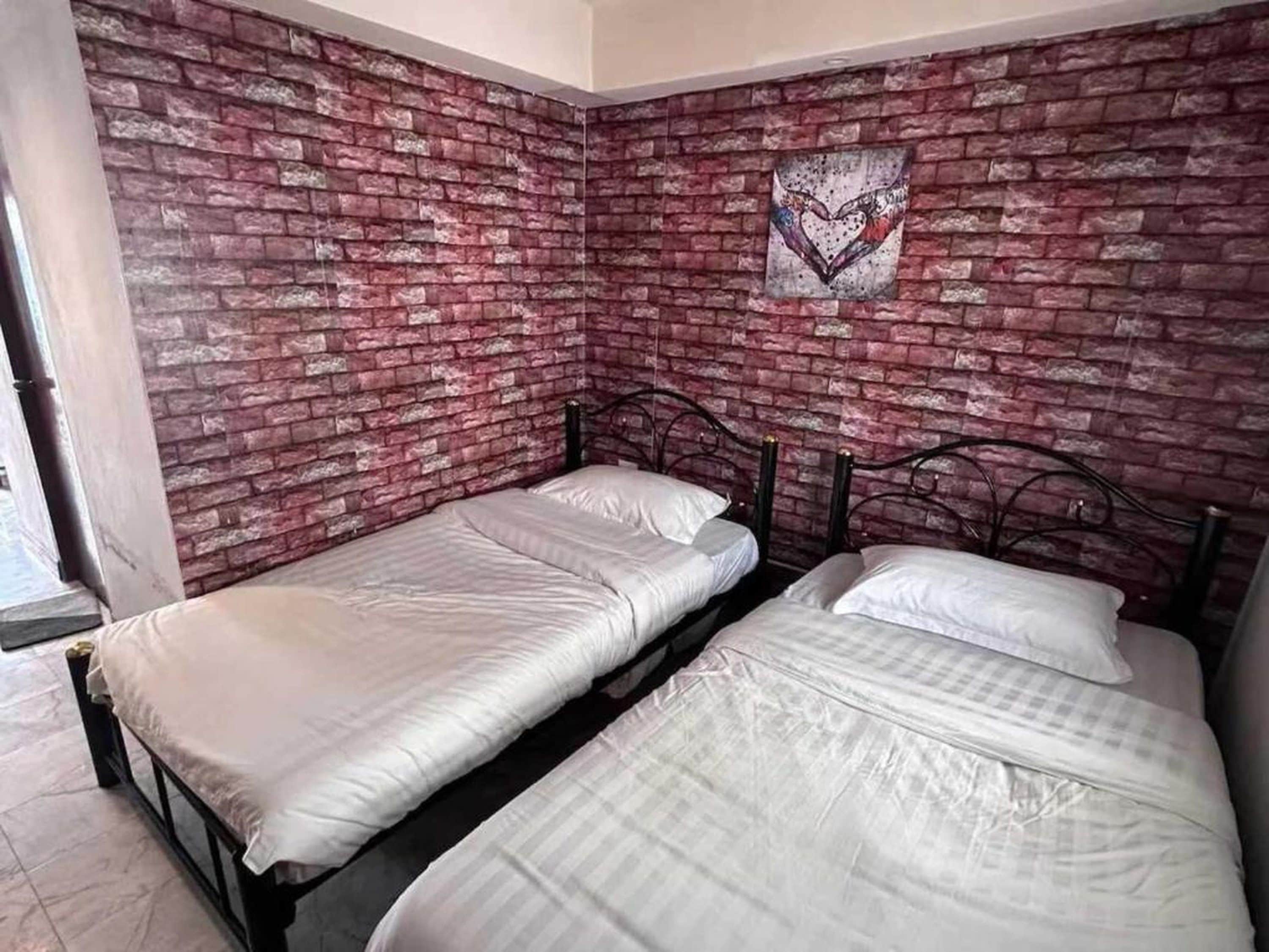 A room with two single beds, a brick-patterned wall, and a heart-shaped artwork.