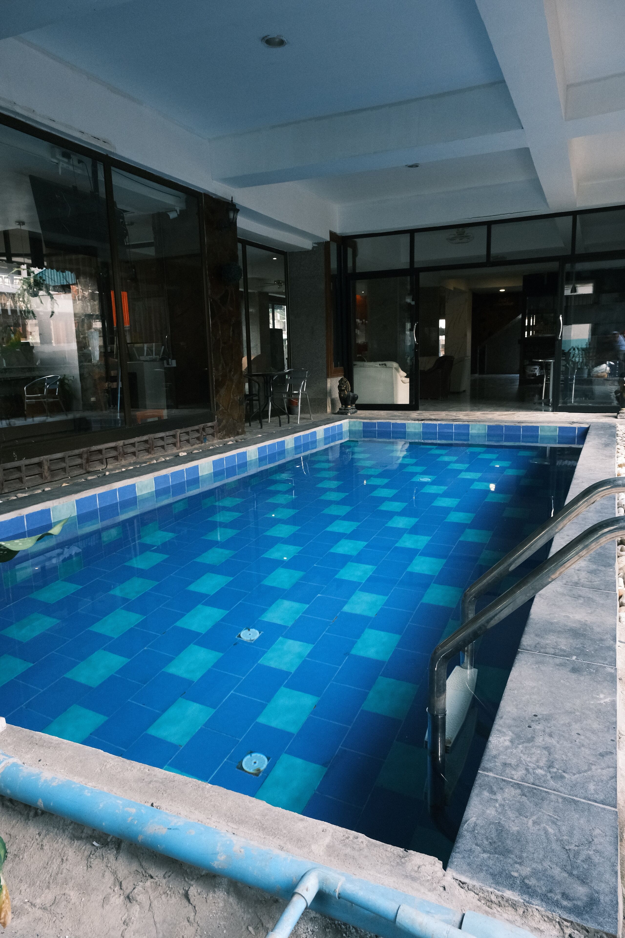 A swimming pool with blue tiles, a glass wall, and a metal ladder.