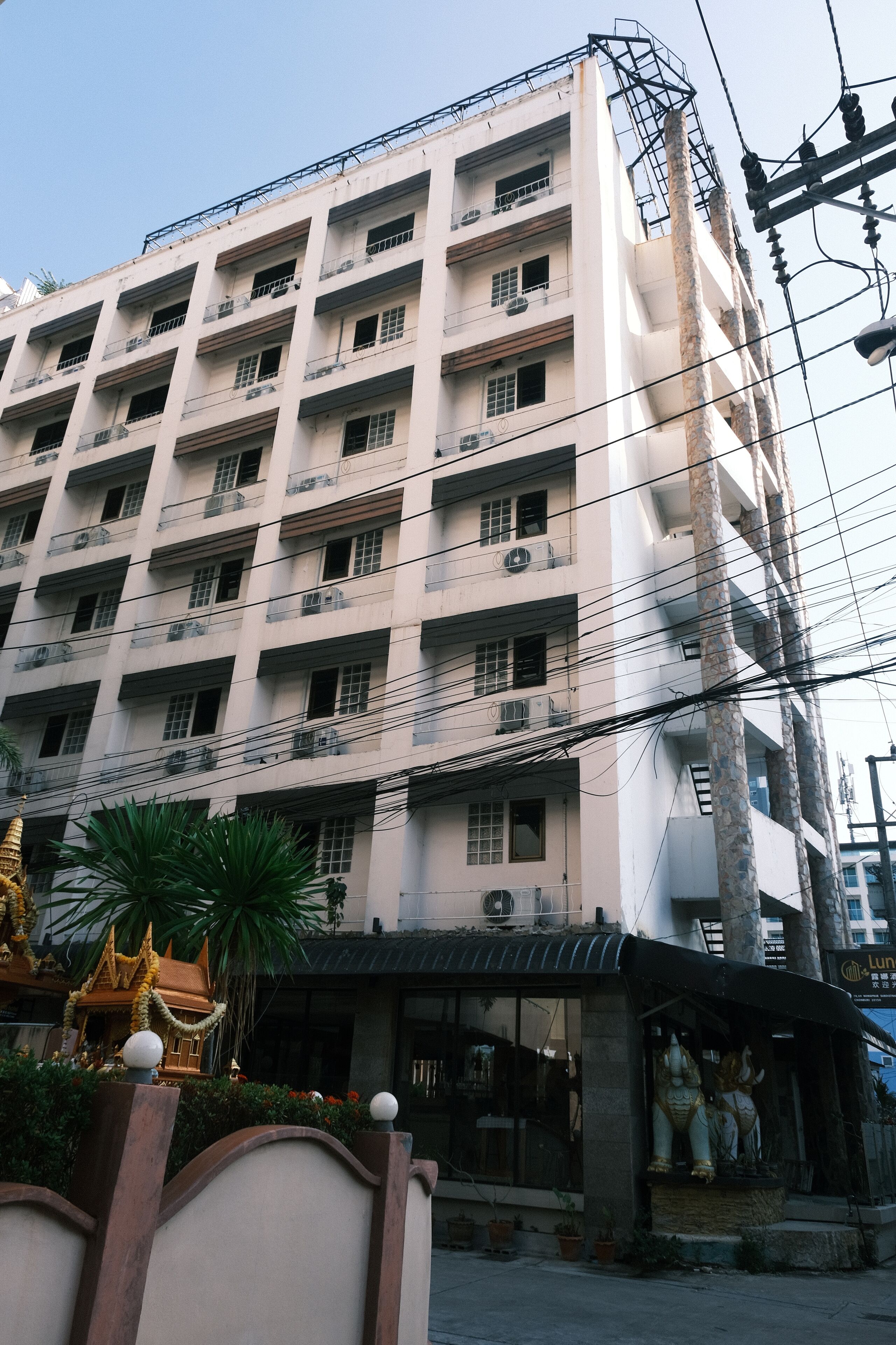 A multi-story building with balconies, a temple-like structure with a golden roof, and a statue in front.