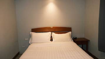 A hotel room with a wooden headboard, a single bed with white bedding, a nightstand, and a wall-mounted light.
