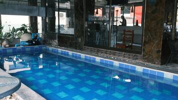 An indoor swimming pool with blue tiles, a stone wall, and a glass door leading to an adjacent room.