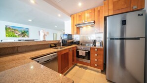 A modern kitchen with granite countertops, wooden cabinets, stainless steel appliances, and a large refrigerator. - Modern 3 BR Condo in PDC - Muuyal 304 (Playa del Carmen)
