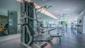 A gym with various exercise machines, a mirrored wall, and large windows providing natural light. - Modern 3 BR Condo in PDC - Muuyal 304 (Playa del Carmen)