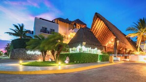 A resort with a thatched-roof building, a stone wall, and well-lit pathways. - Modern 3 BR Condo in PDC - Muuyal 304 (Playa del Carmen)