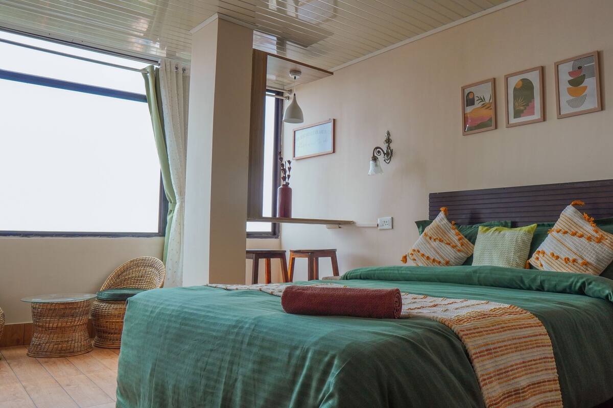 A bedroom with a bed, green bedding, a headboard, and a window with curtains.