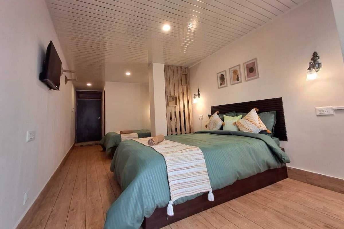 A bedroom with a wooden floor, a bed with green bedding, a wooden headboard, and a wall-mounted TV.