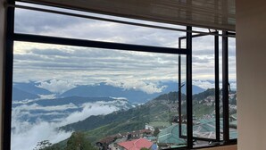 A room with a large window overlooking a mountainous landscape with a town below. - Monratino Himadrie (Darjeeling)