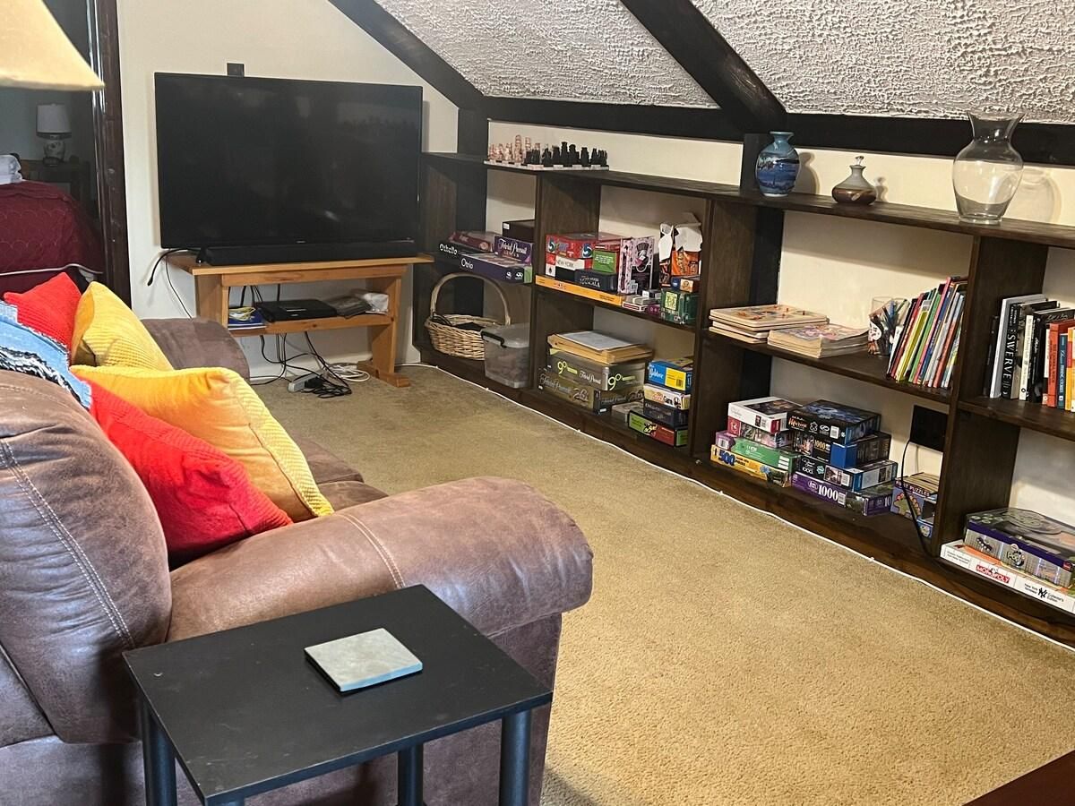A living room with a leather sofa, a television on a stand, and a bookshelf filled with books and board games.