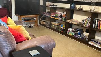 A living room with a leather sofa, a television on a stand, and a bookshelf filled with books and board games.