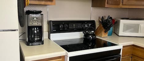 Una cocina con estufa, microondas, cafetera y armarios de madera.
