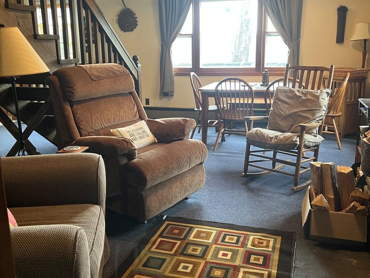Un salon chaleureux avec un canapé en cuir marron, un fauteuil à bascule et un tapis à motifs.