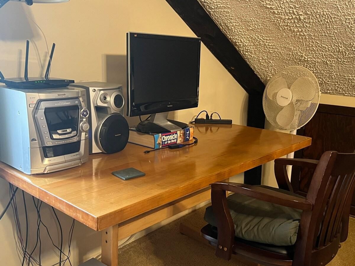 Un escritorio de madera con un monitor de computadora, un altavoz, un microondas y un libro titulado 'Chronicle of the World'.