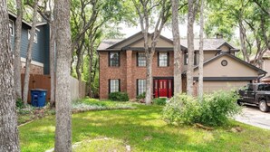 A two-story house with a red door, a garage, and a driveway. - Tranquil Family Retreat in NW Austin, Hot Tub, Office, & Backyard Escape (Austin)