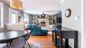 A modern living room with a fireplace, a dining area with a round table, and a kitchen area with built-in shelves. - Tranquil Family Retreat in NW Austin, Hot Tub, Office, & Backyard Escape (Austin)