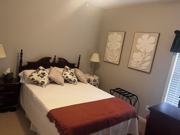 A neatly made bed with floral pillows, a bedside lamp, and a nightstand with a tissue box. - Charming 3-bed, 2-bath house in Mableton with Wi-Fi, seasonal pool, firepit (Mableton)